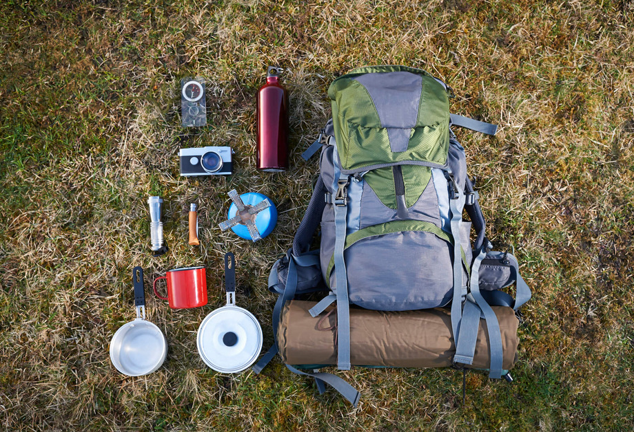A flat lay image of camping essentials along with a backpack on a grass background