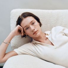 Woman leaning on white chair wearing white v-neck shirt and gold earrings.