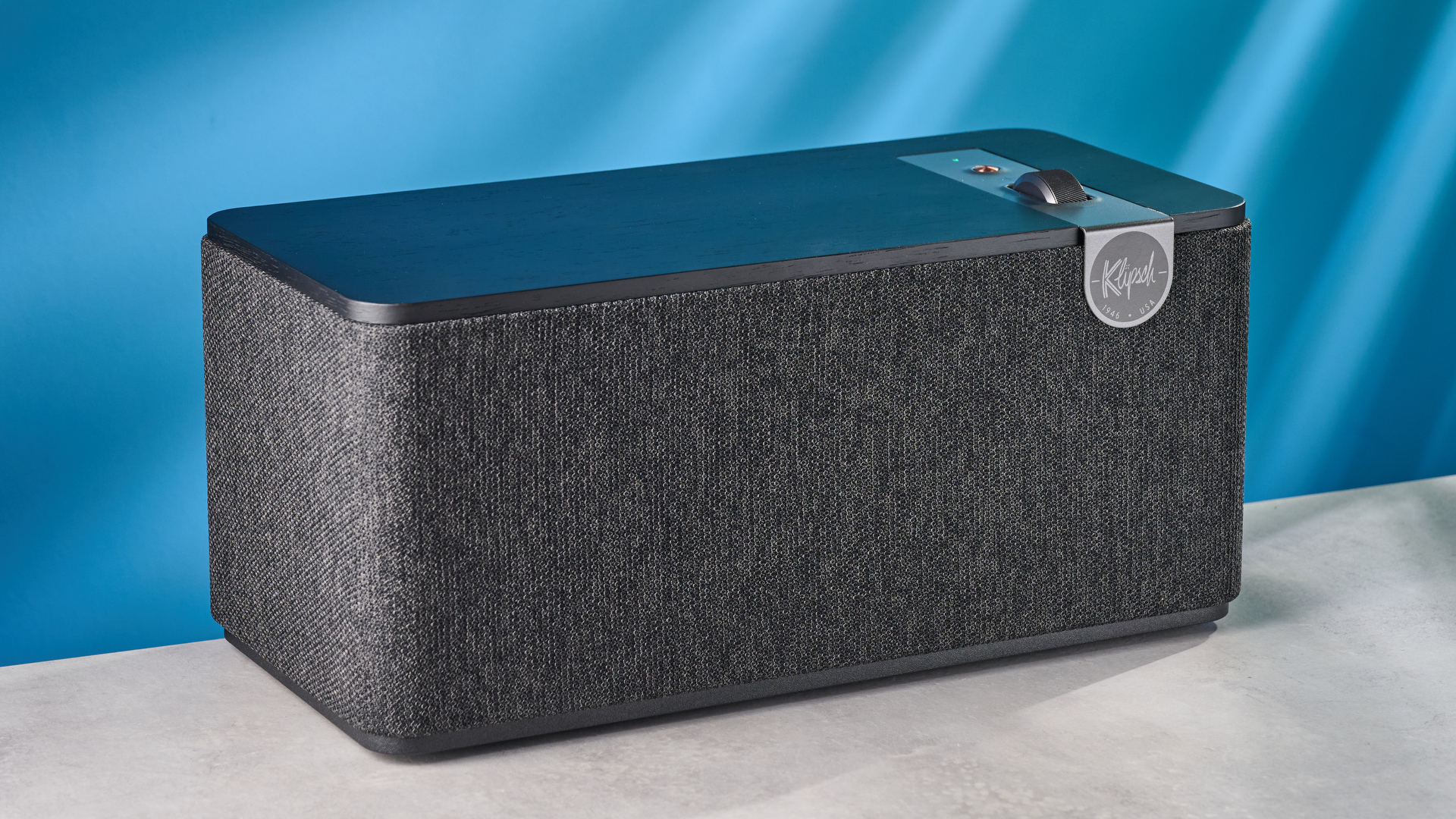 Klipsch The One Plus Bluetooth speaker in matte black photographed in front of a blue background.