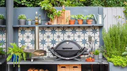 Corner of garden with tabletop BBQ, festoon lighting and potted plants