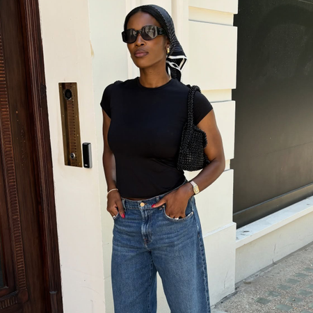 Woman wearing black t-shirt, black sunglasses, silk scarf, and mid-wash barrel leg jeans.