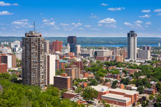 a cityscape of moderate and some tall buidlings. off in the distance some water and a forest of green.