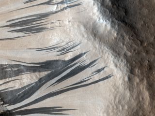 Slope streaks in Acheron Fossae on Mars. What creates these dark streaks is a puzzle, but one hypothesis is that they are caused by fine-grained sand sliding down the banks of troughs and craters.