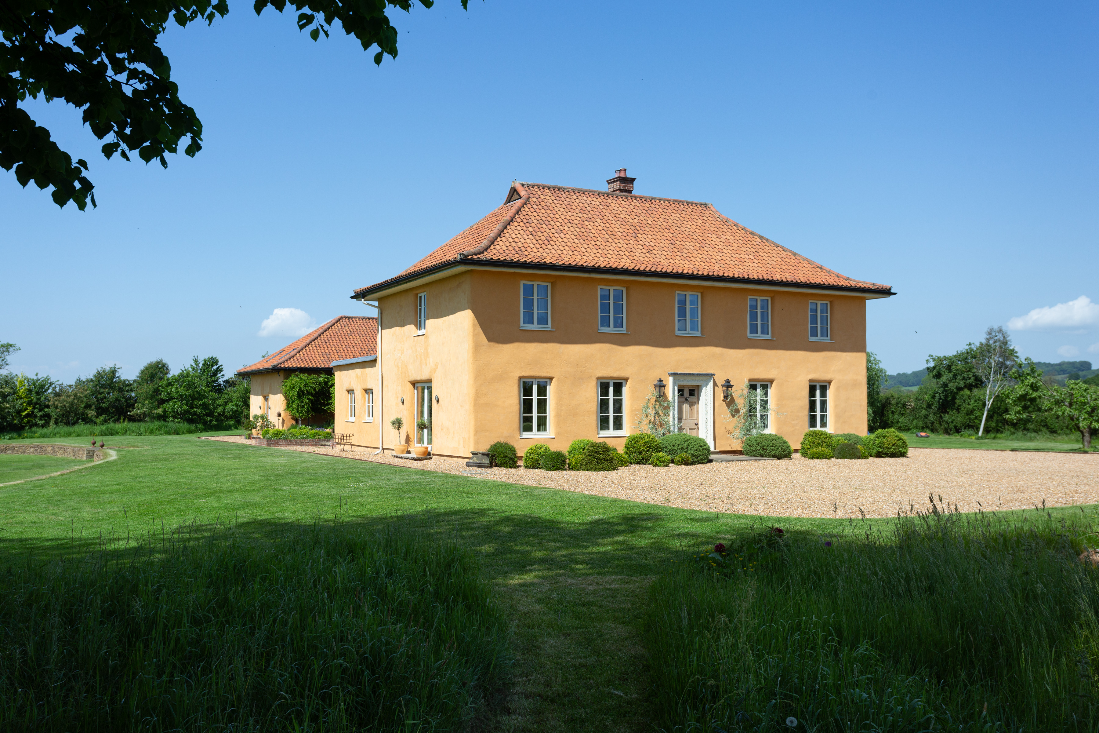Details of the Lime House in Yorkshire. It is yellow, with a red tiled roof surrounded by green fields. Inside, wood panelled walls contrast with stone fittings and floors for a very farmhouse feel.
