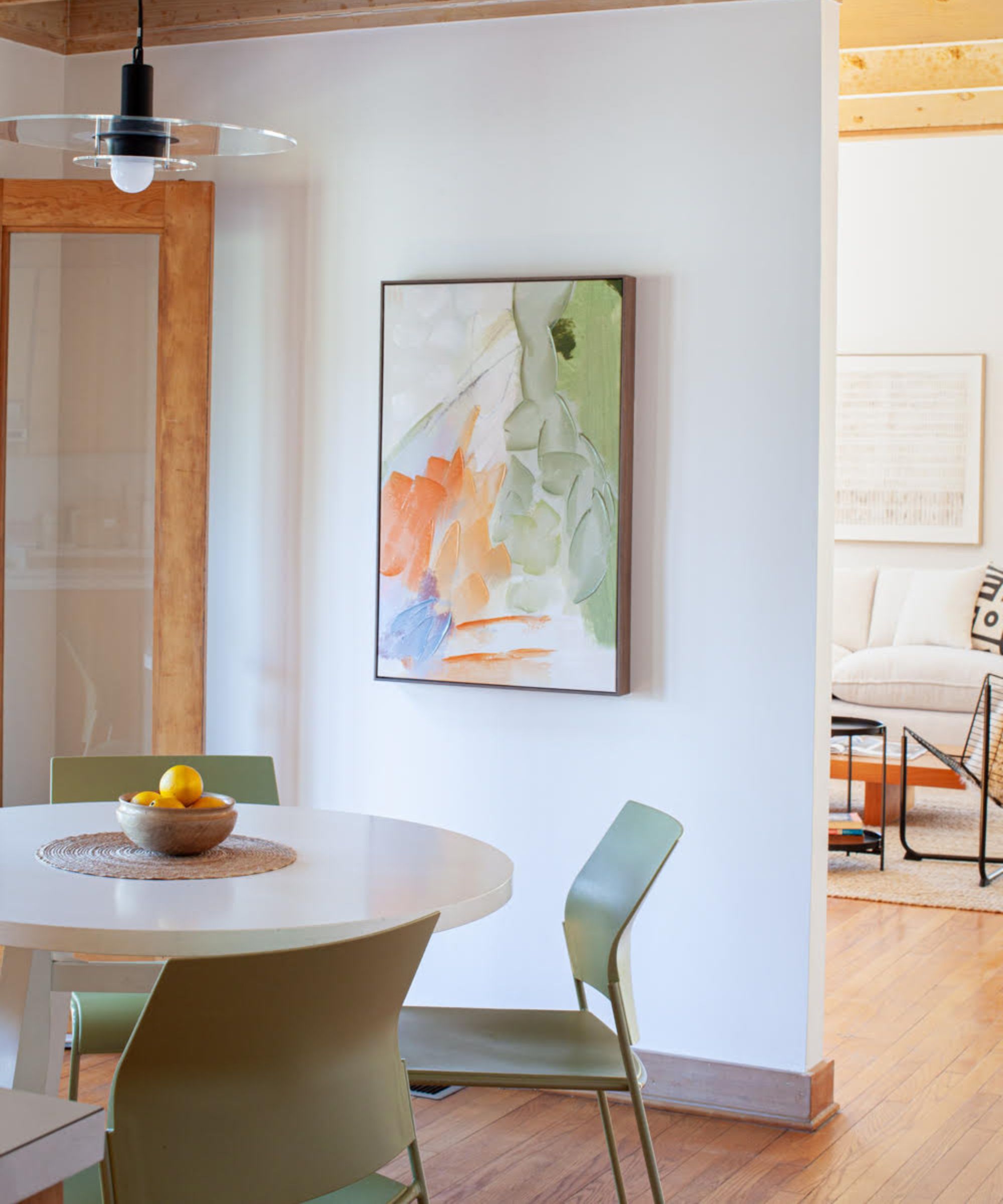 A corner of a small kitchen with an eat-in area created using a round white table, four green chairs, and a glass pendant light