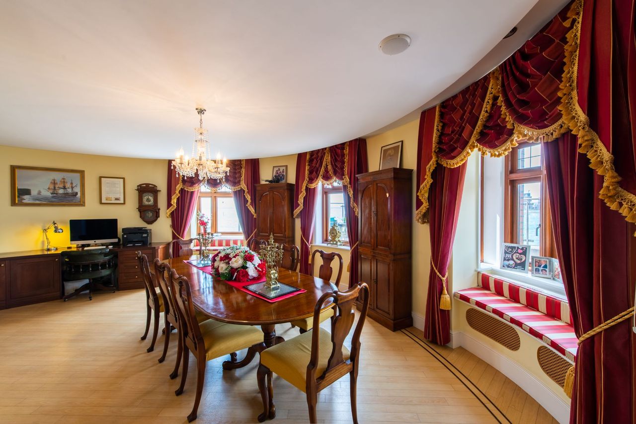 The dining room has wooden flooring and windows sills and claret curtains