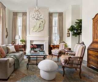 living room with pale stone fireplace cream artwork and striped armchairs and mushroom stool