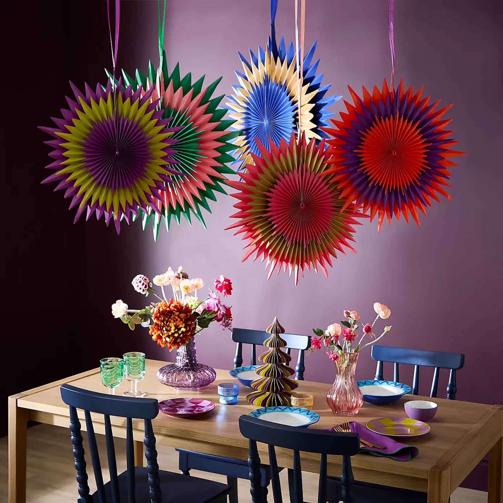 Dunelm Pack of 5 Sophie Robinson Folding Prism Star Paper Fans hung above a dining table