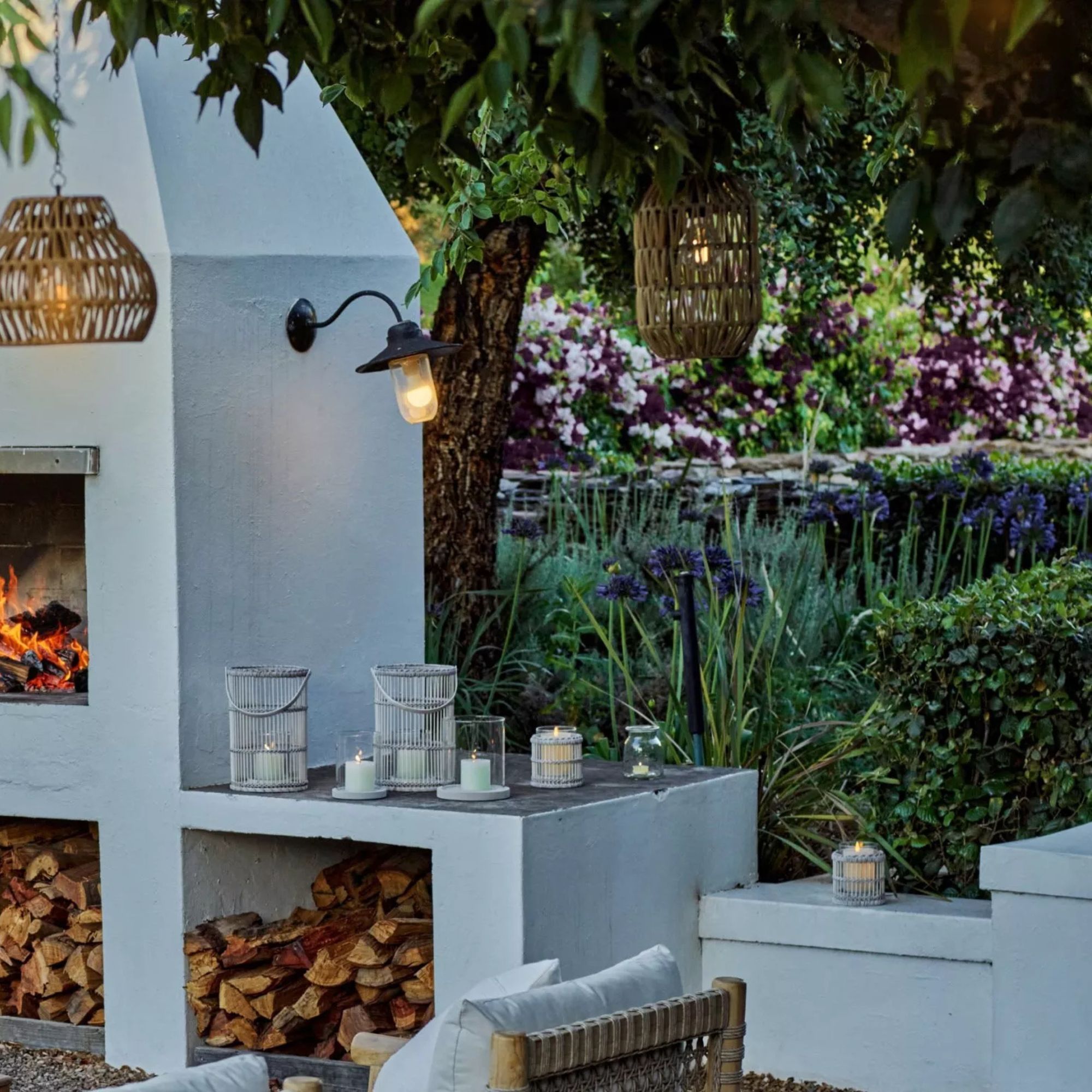 The White Company garden setup with large white wood burner with logs, hanging lights and florals