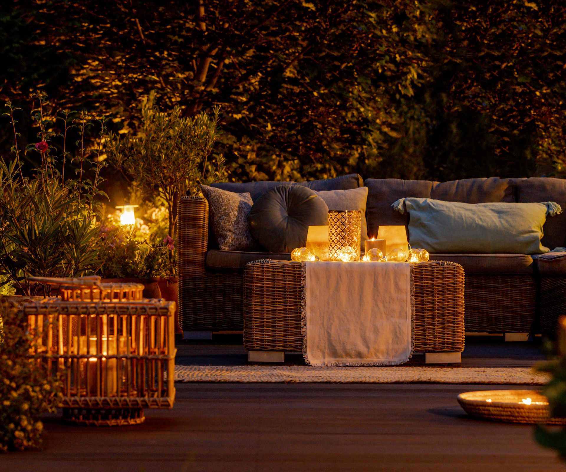 night-time patio with ambient lighting, sofa, chairs and table, with hedge behind