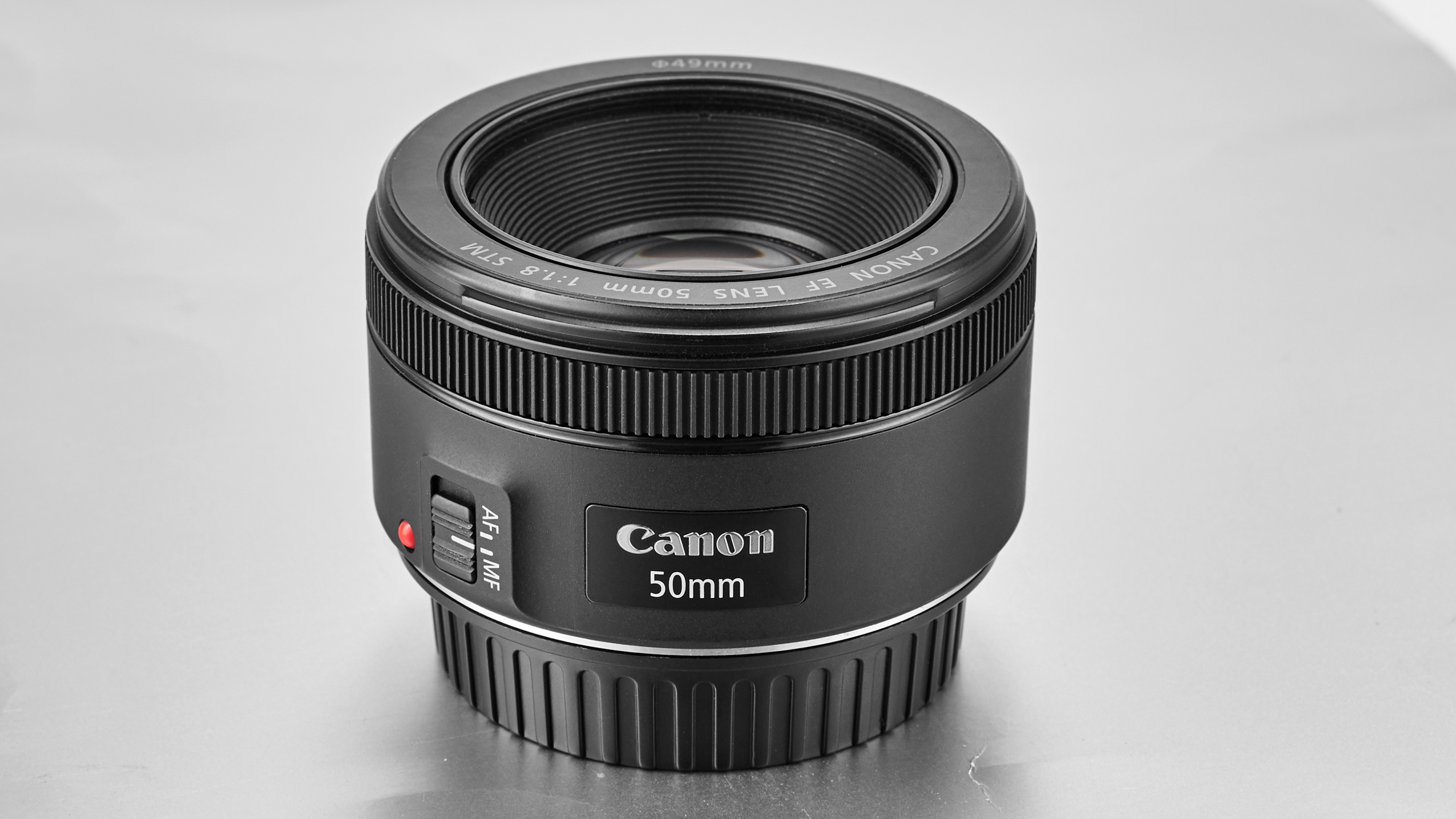 Canon EF 50mm f/1.8 STM camera lens with autofocus/manual focus switch, placed on a light-reflective surface