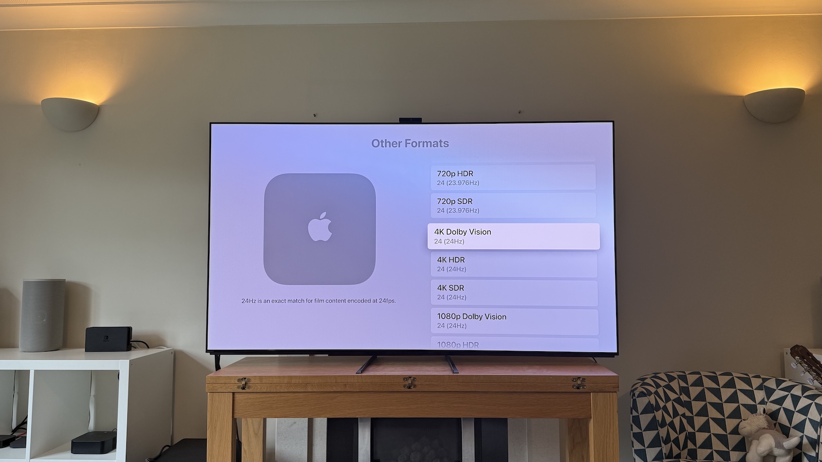 A photo of the 65-inch Sony A95L TV on wooden table in a living room. On the screen is the Apple TV 4K's 'Other Formats' menu.