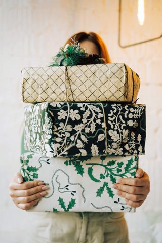 Portrait of a long-haired red-haired woman with gifts packed in white and green boxes. Christmas holidays, meeting the New year. Zero waste concept, recyclable cardboard, craft. Festive pre-Christmas mood, garlands, cozy atmosphere.