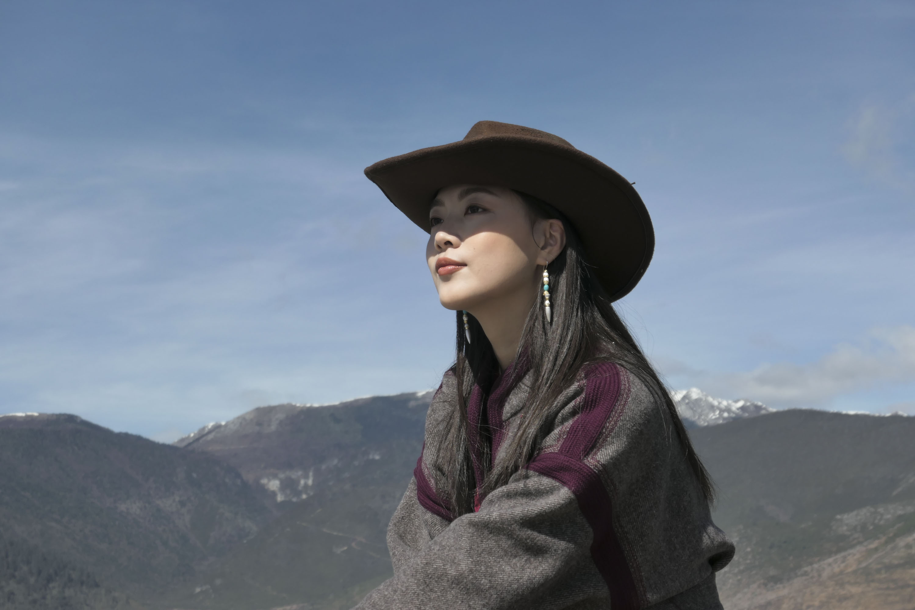 A portrait of a woman in a cowboy hat with a snowy mountain backdrop