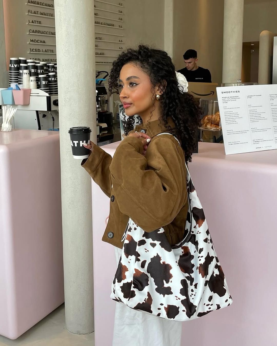 Influencer in brown jacket cream trousers, white scrunchie and a cow print hobo bag.