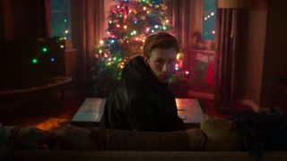 Hector Newman (Luther Ford) sits on a couch in front of a Christmas tree, in 'Black Doves.'