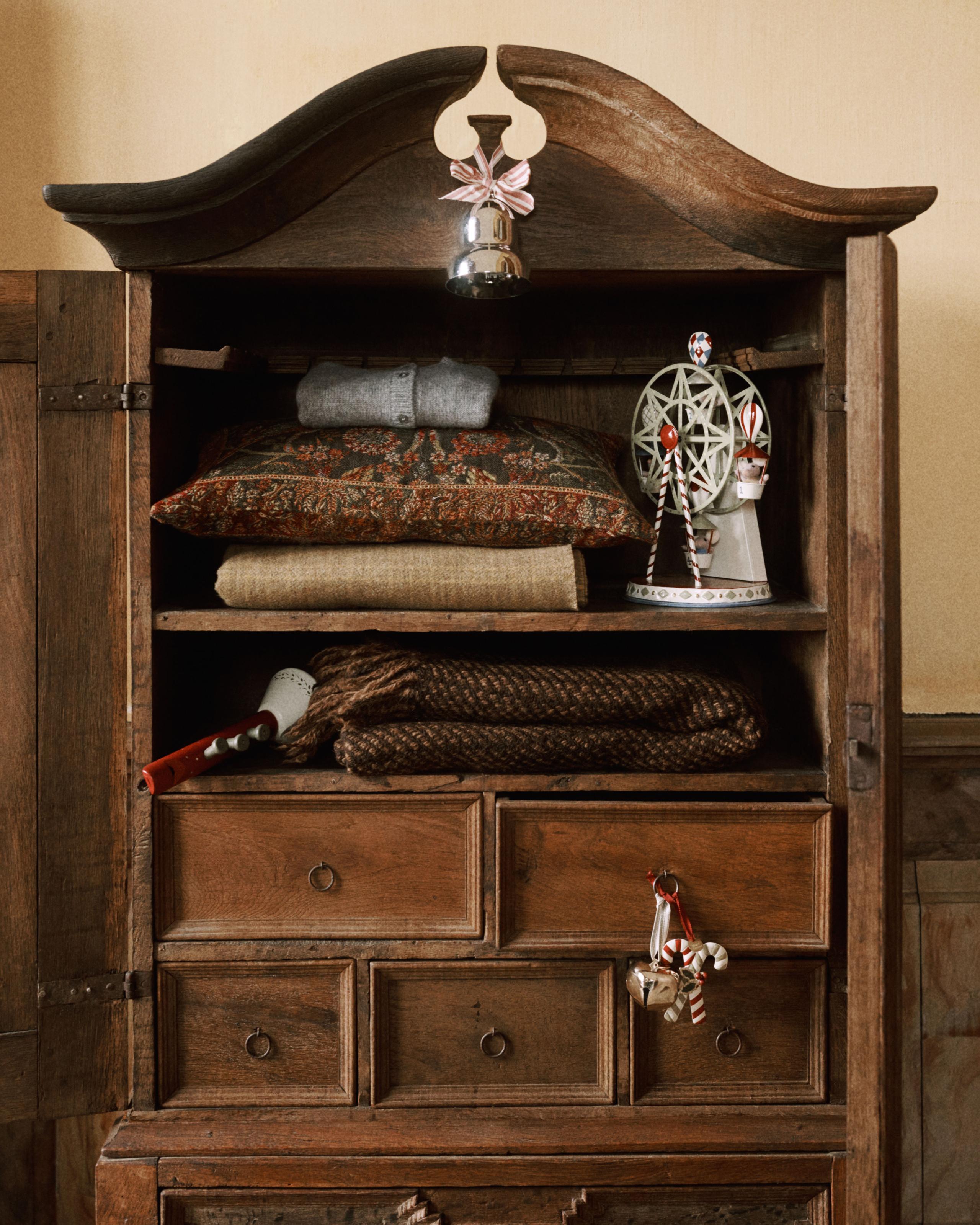 Image of a vintage wooden wardrobe filled with cozy blankets and vintage Christmas ornaments.