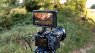 An Atomos Shinobi II camera monitor on top of a camera outside in a field