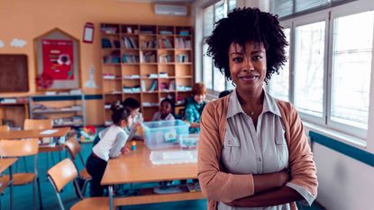 black woman with curly hair, arms crossed standing in front of elementary students