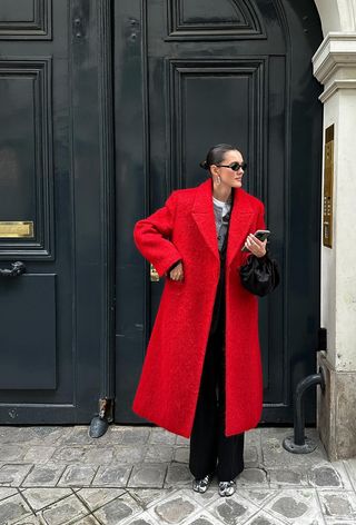 a photo showing what colors go with red, specifically a woman wearing a red coat and gray cardigan and black trousers and silver heels