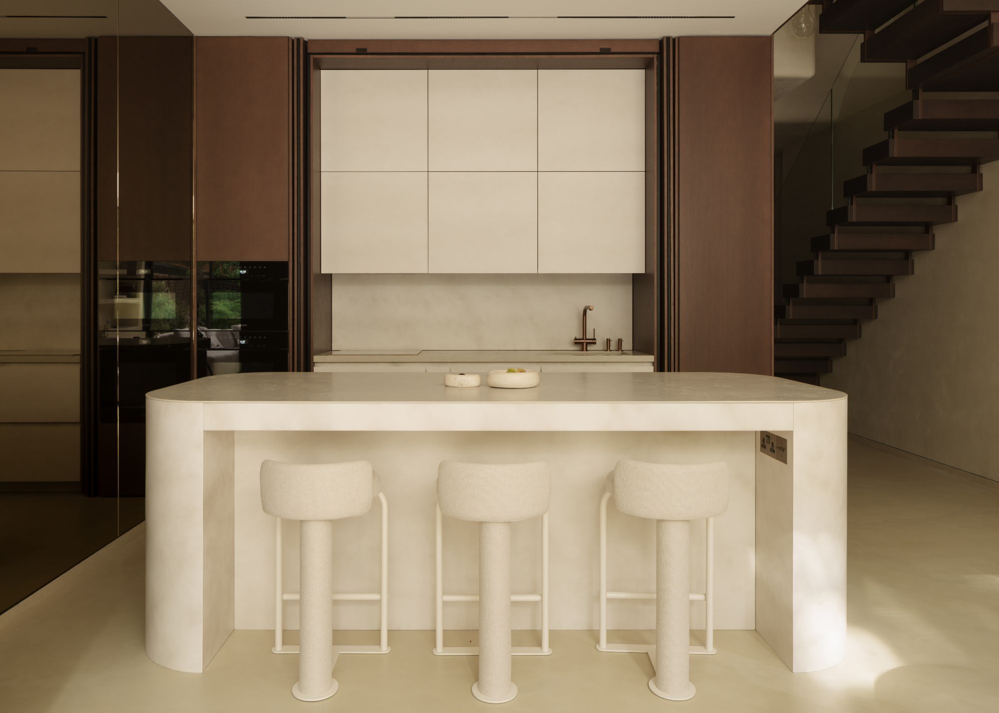 A rounded, cream-colored marble kitchen island with three cream bar stools, in front of a marble cream kitchen area that can be hidden away with sliding timber doors
