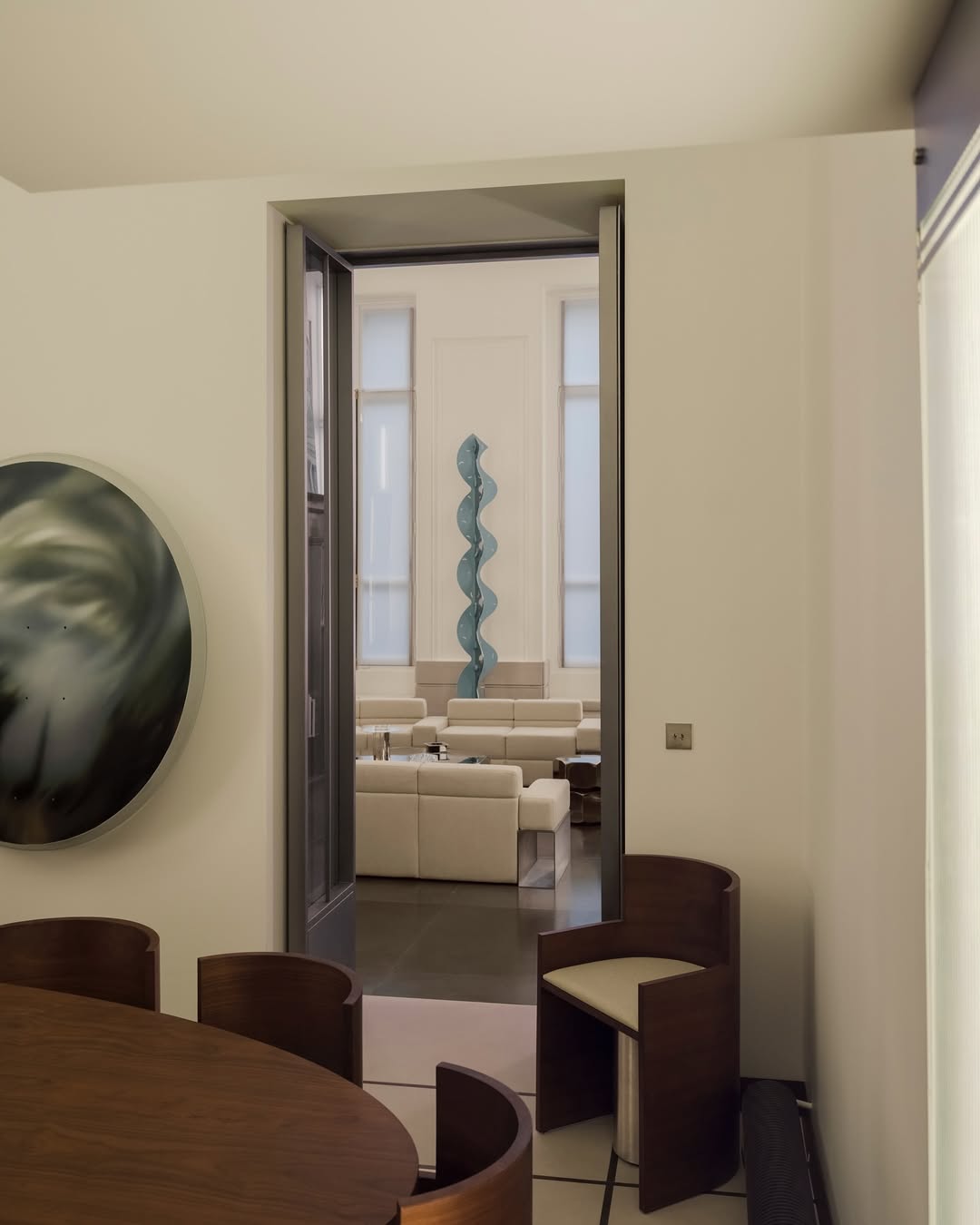 A beige, wood, and chrome-tinted contemporary apartment filled with sculptural furnishings, including geometrically cut tables, sofas, and chairs, abstract artworks, and upholstered sofas.