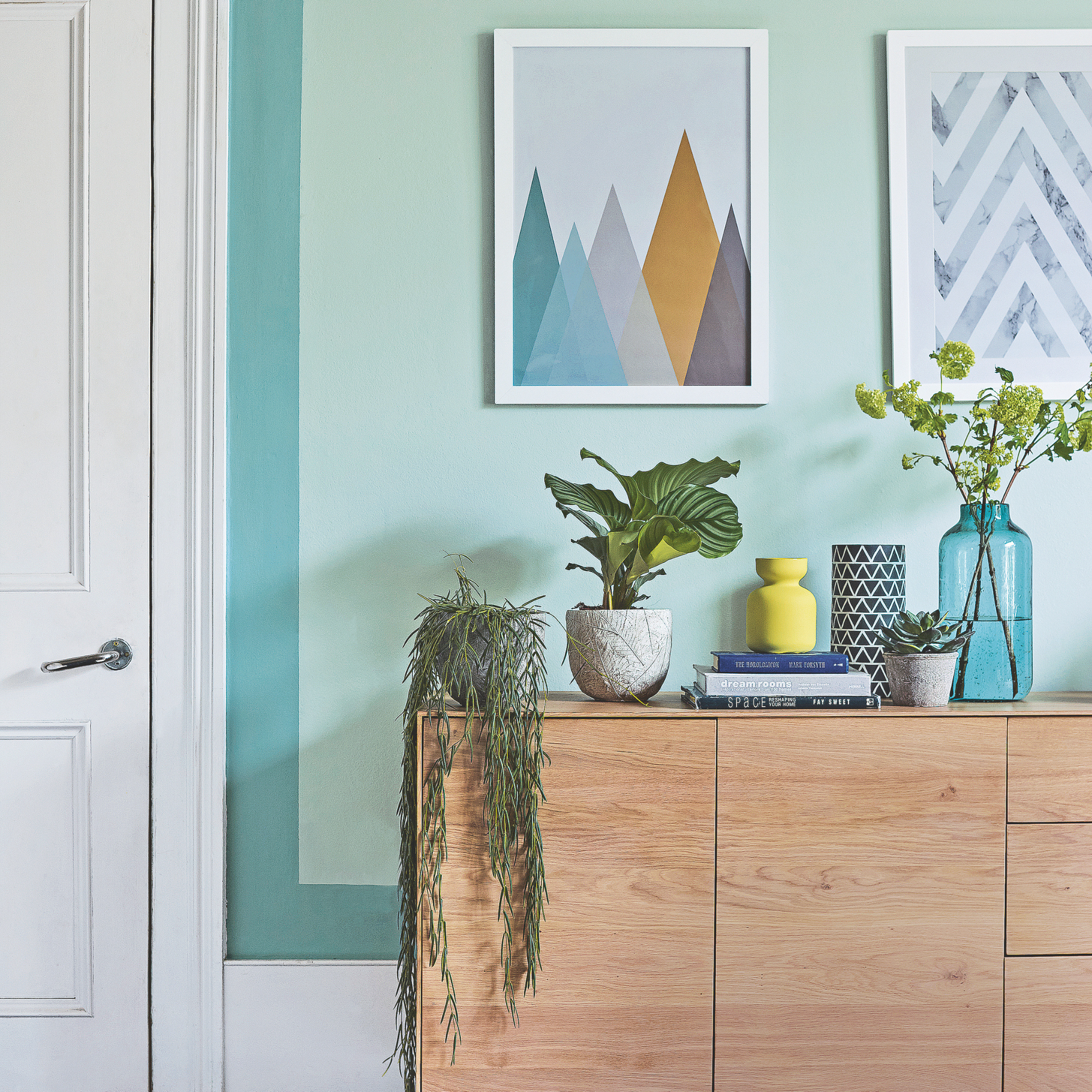 Living room with black painted floor, mint green walls and wooden sideboard.