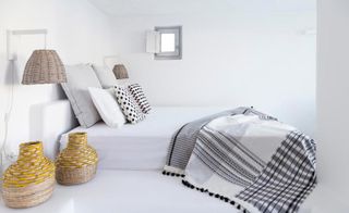 Bedroom featuring a bed with white bedspread, black and white cushions and throw, and wicker baskets and lightshades