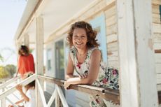 Portrait of a smiling, confident woman in her 50s on a sunny beach hut patio.