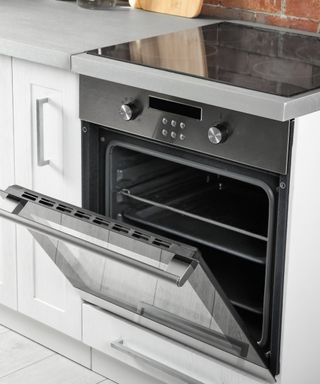 An image of an oven with an open door in a white and gray kitchen with redbrick walls