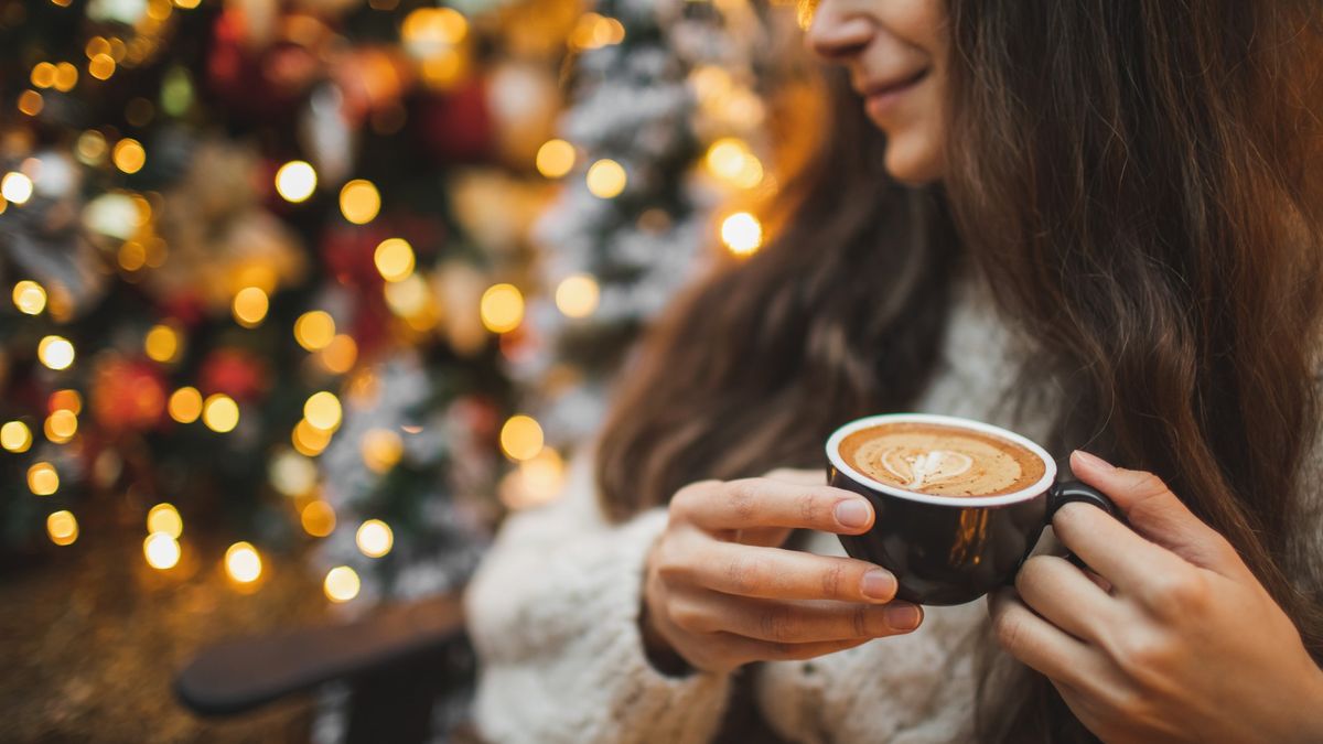 Woman sitting beside Christmas tree holding cup of coffee