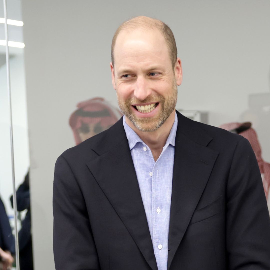 Prince William wearing a suit and laughing standing in a room with gamers