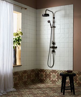 A shower room with white wall tiles and patterned encaustic floor tiles