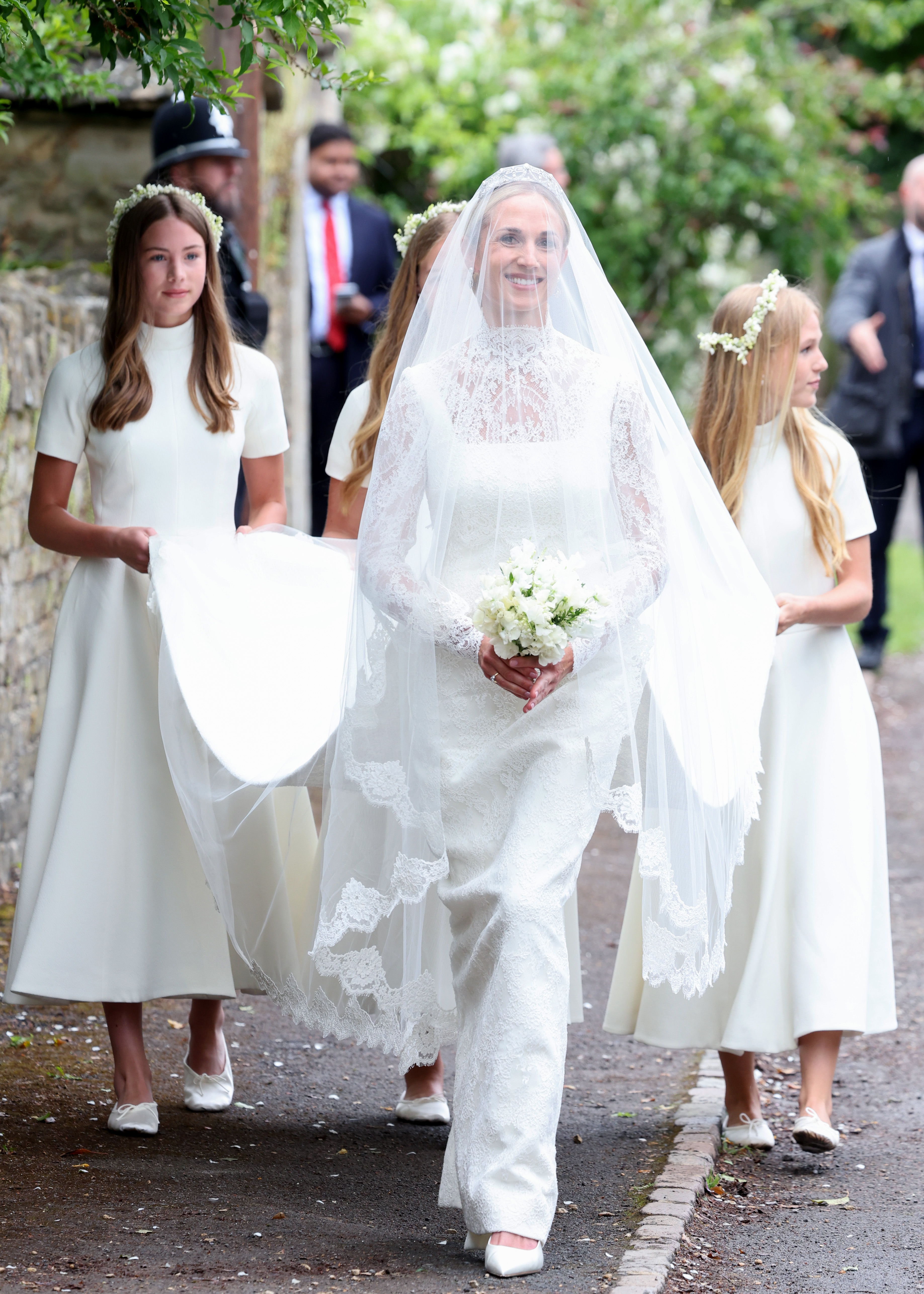 Harriet Sperling arrives at her royal wedding to Princess Anne's son wearing a white column gown featuring long lace sleeves, a tiara, and a long veil