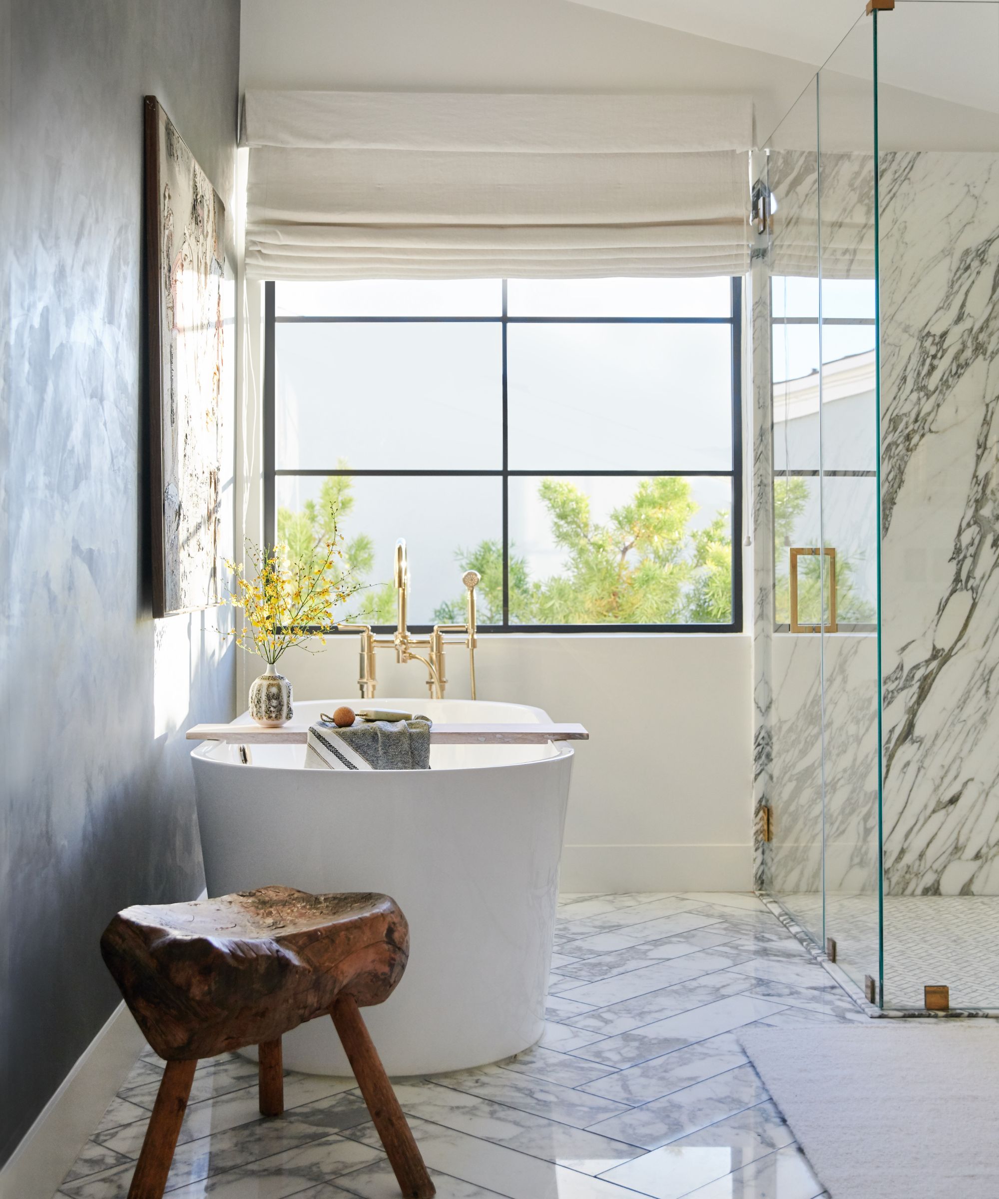 A white bathroom with marble floors, a large glass shower enclosure, and a freestanding bath beneath a large window