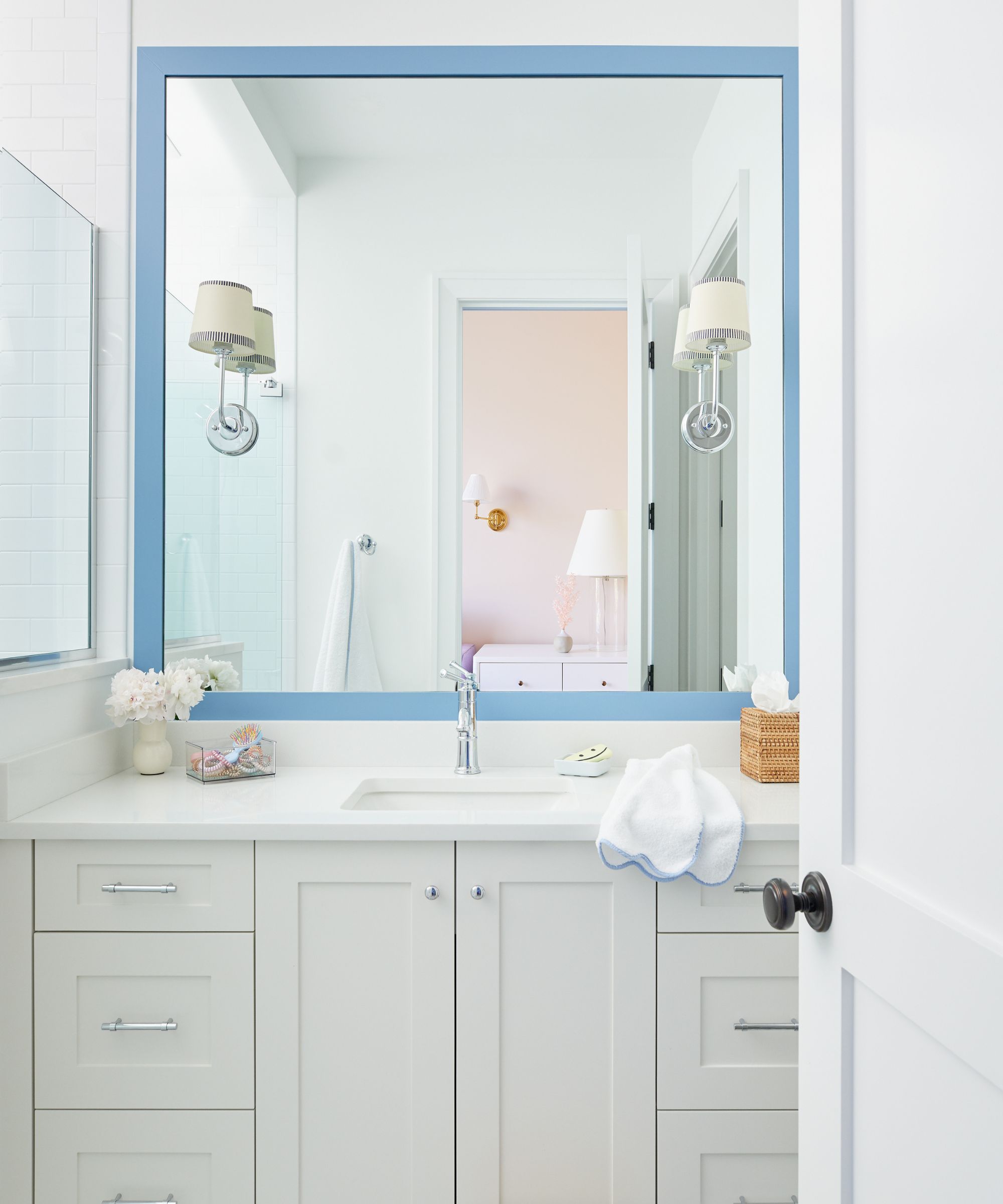 A small coastal bathroom with white walls, and white vanity, and blue framed mirror and two sconces installed into the mirror