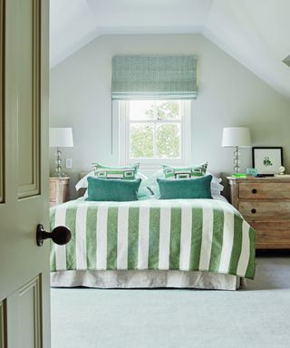 bedroom with green striped throw, green cushions, green roman blind and wooden chests of drawers