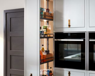 Pull-out storage unit with white cabinets next to a built-in oven