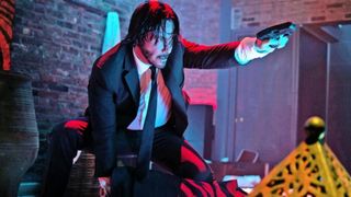 John Wick (Keanu Reeves) crouches on a table as he points a gun.