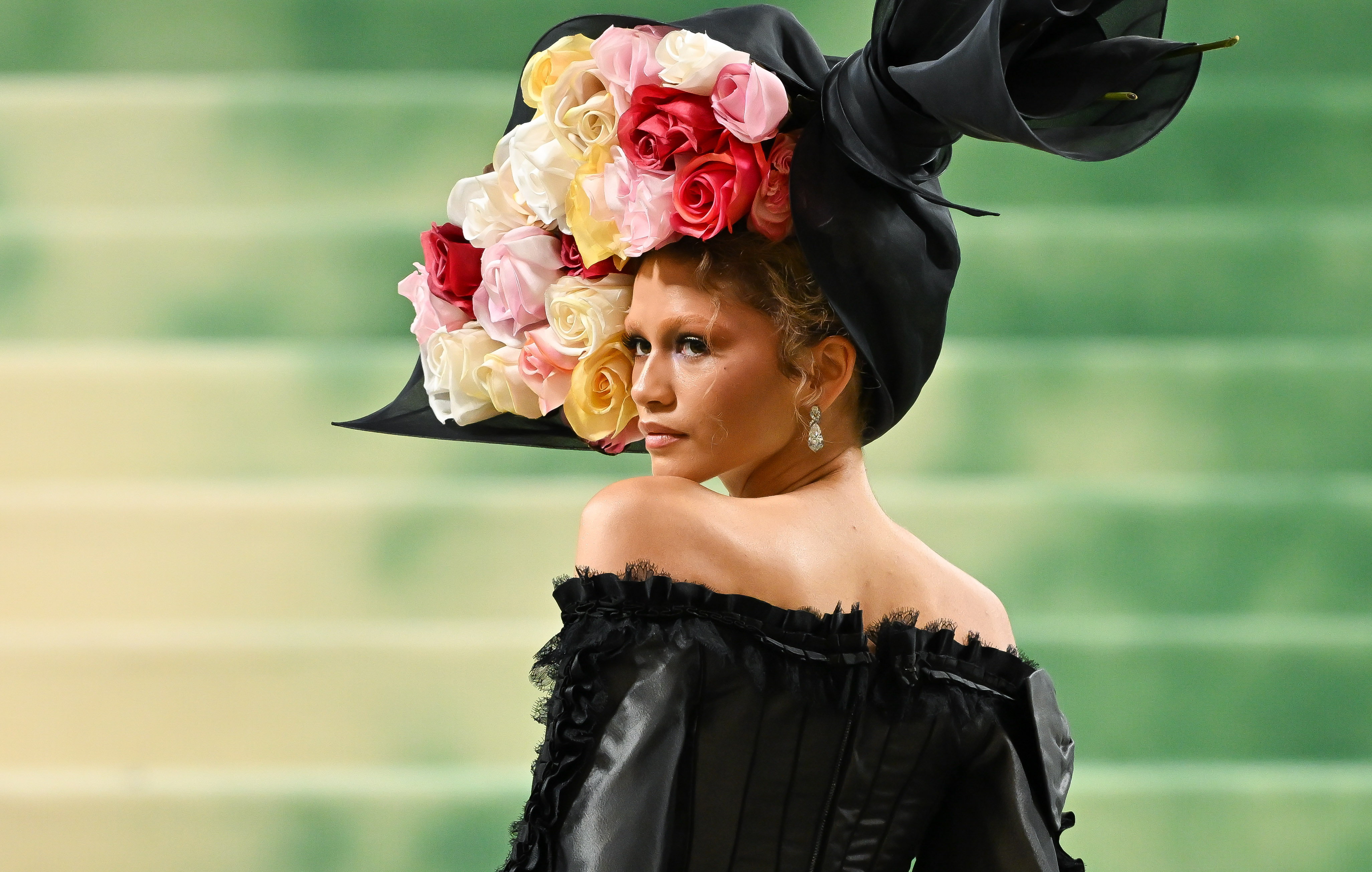 Zendaya posing on the Met Gala red carpet in a black off the shoulder dress and large floral headpiece