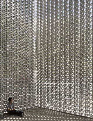 Man sitting on the floor next to metal screen walls casting shadows