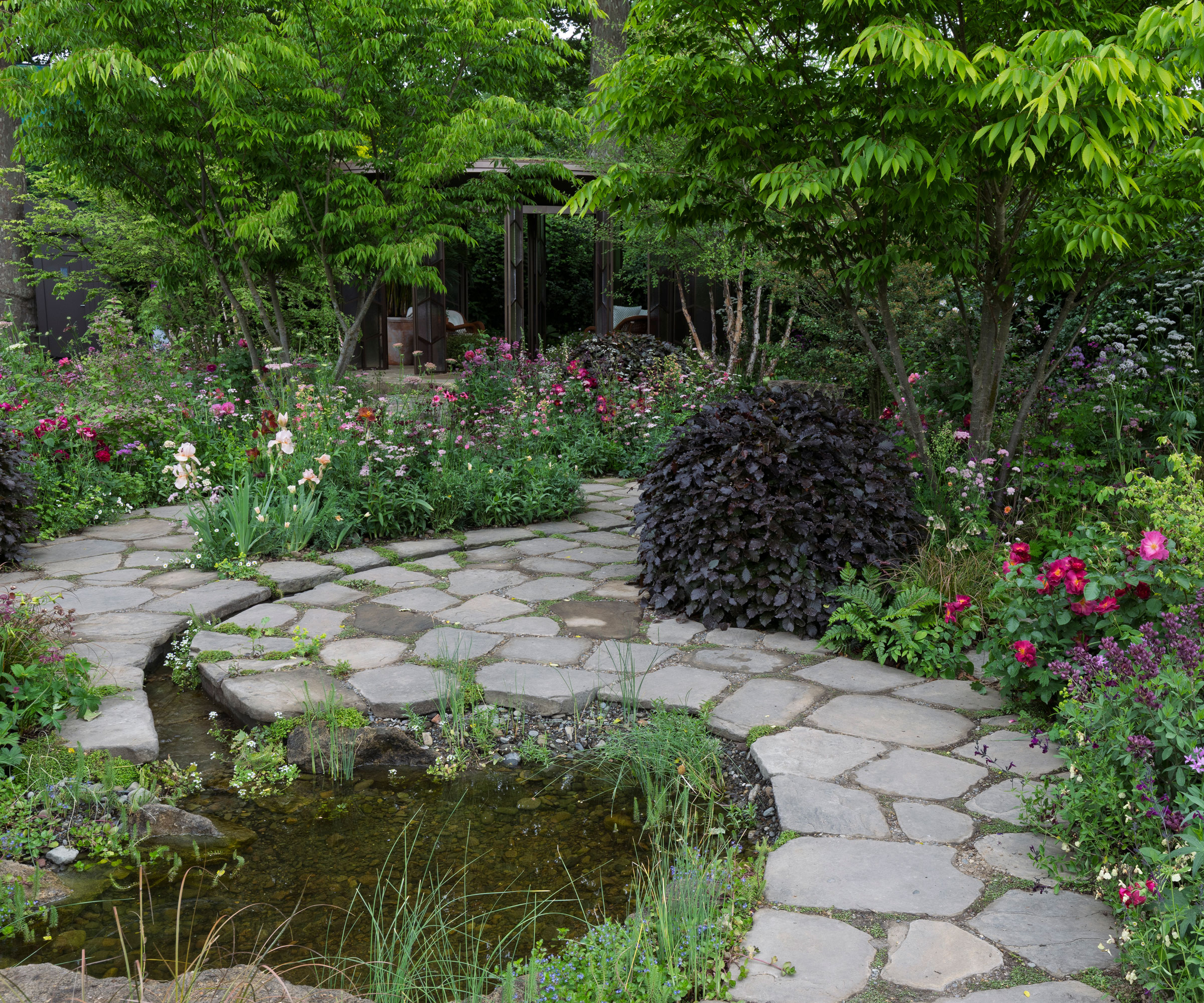 natural garden pond design with winding path in crazy paving, plants and trees
