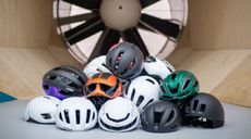 A stack of aero helmets sit on the floor in front of a wind tunnel fan