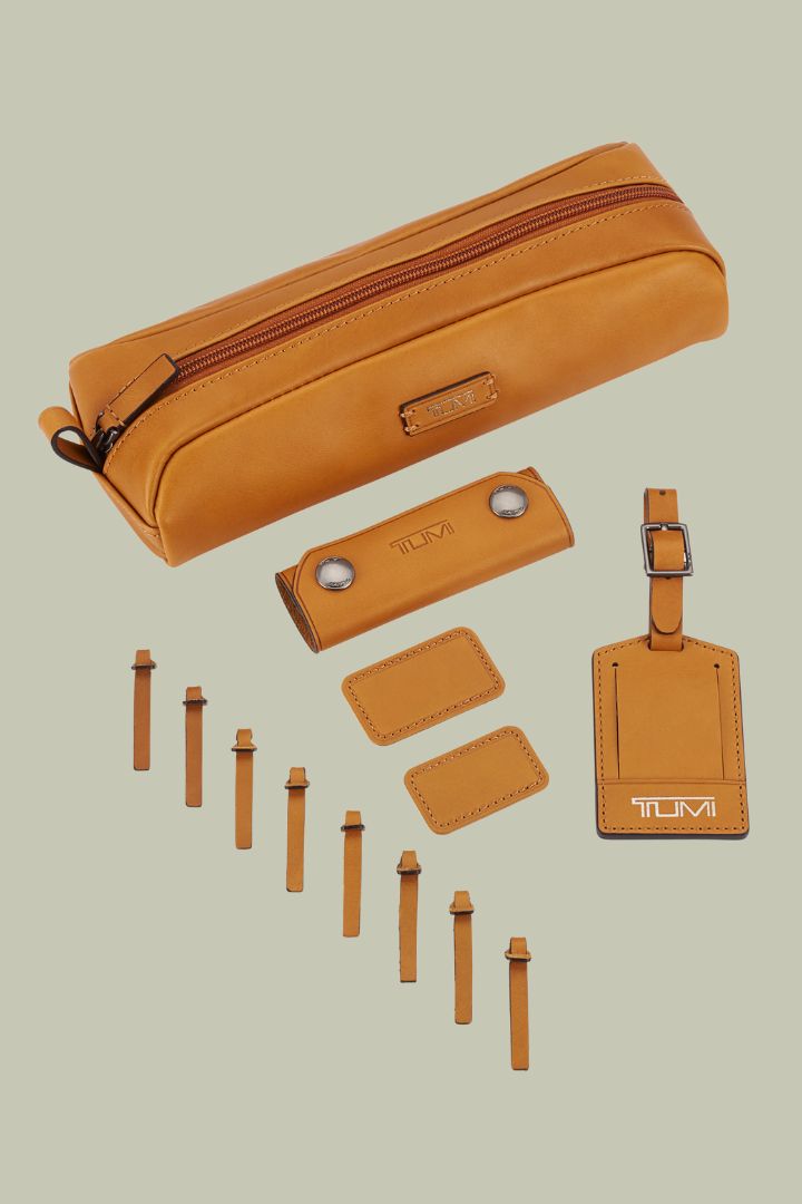 A series of brown leather travel accessories, embossed with the logo TUMI, against a pale green background.