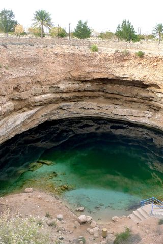 The Bimmah Sinkhole is near Dibab village in Oman, an Arab state in the Arabian Peninsula. A winding stone staircase leads down to the sinkhole, which is a beautiful aquamarine and emerald color, with the darker green hues resulting from algae growth in the water.
