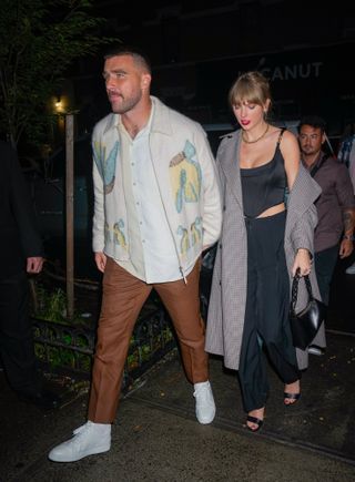 Taylor Swift wearing a black corset top with black trousers and a long grey coat
