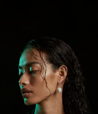 Woman wearing a single dangling pearl earring against a black background