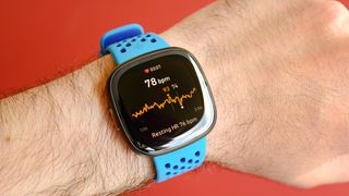 The Fitbit Sense 2 on a blue rubber strap, shown on a user's wrist against a red background.