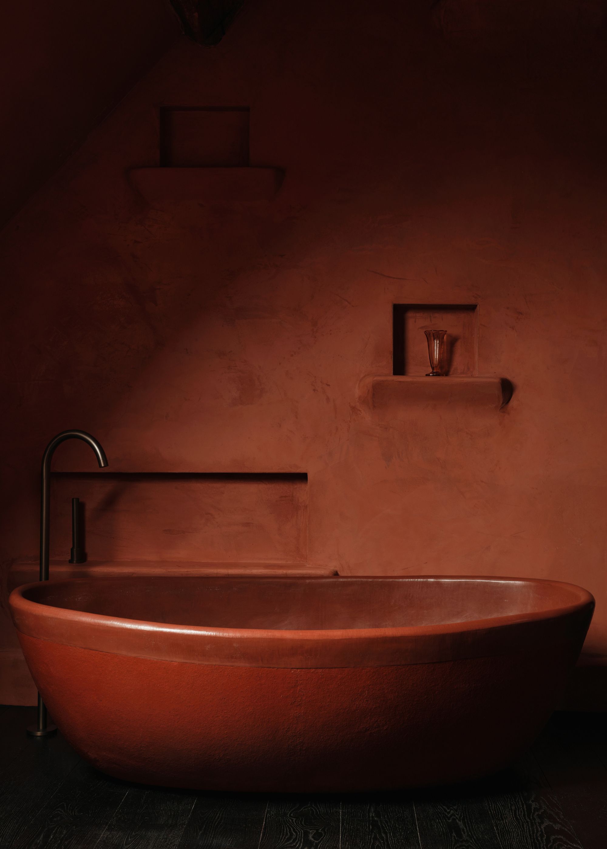 A deep red bathroom with a red bathtub in the middle and deep red painted walls.