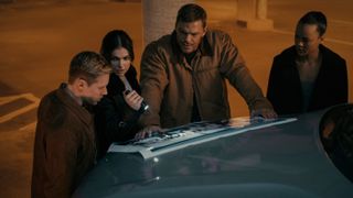 Reacher and the other 110th members looking at a staff photo on the hood of an SUV in Reacher season 2 episode 3.